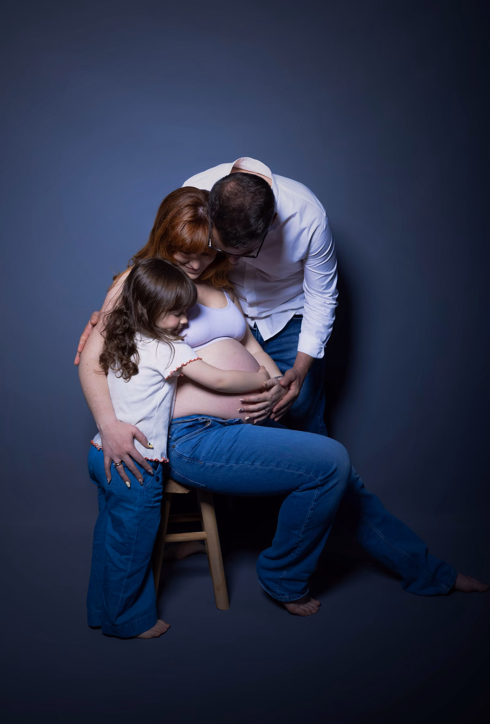 Les parents et leur fille aînée blottis autour du ventre, assis sur un tabouret