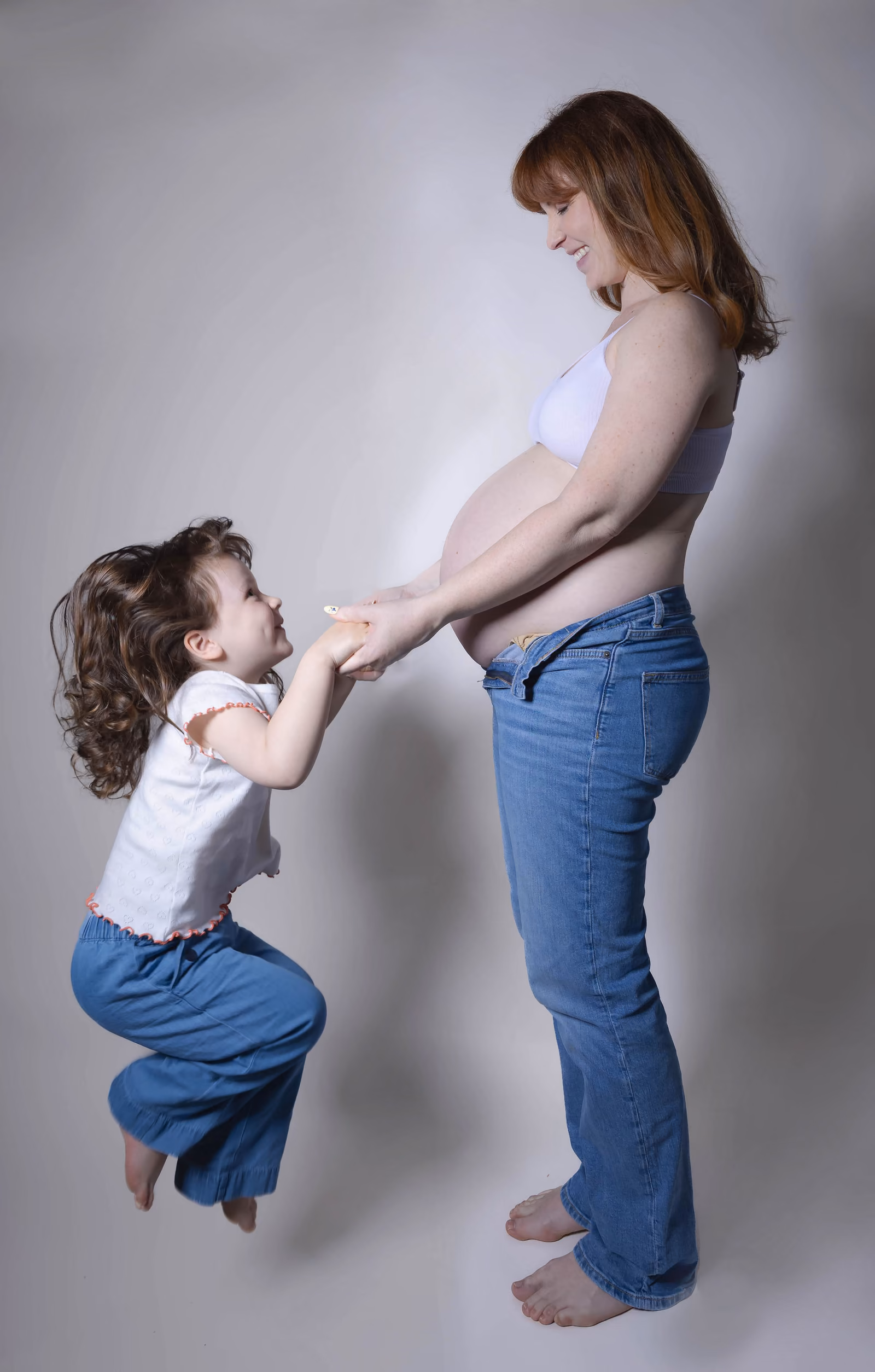 La petite fille tend les mains vers le ventre de sa maman, en studio