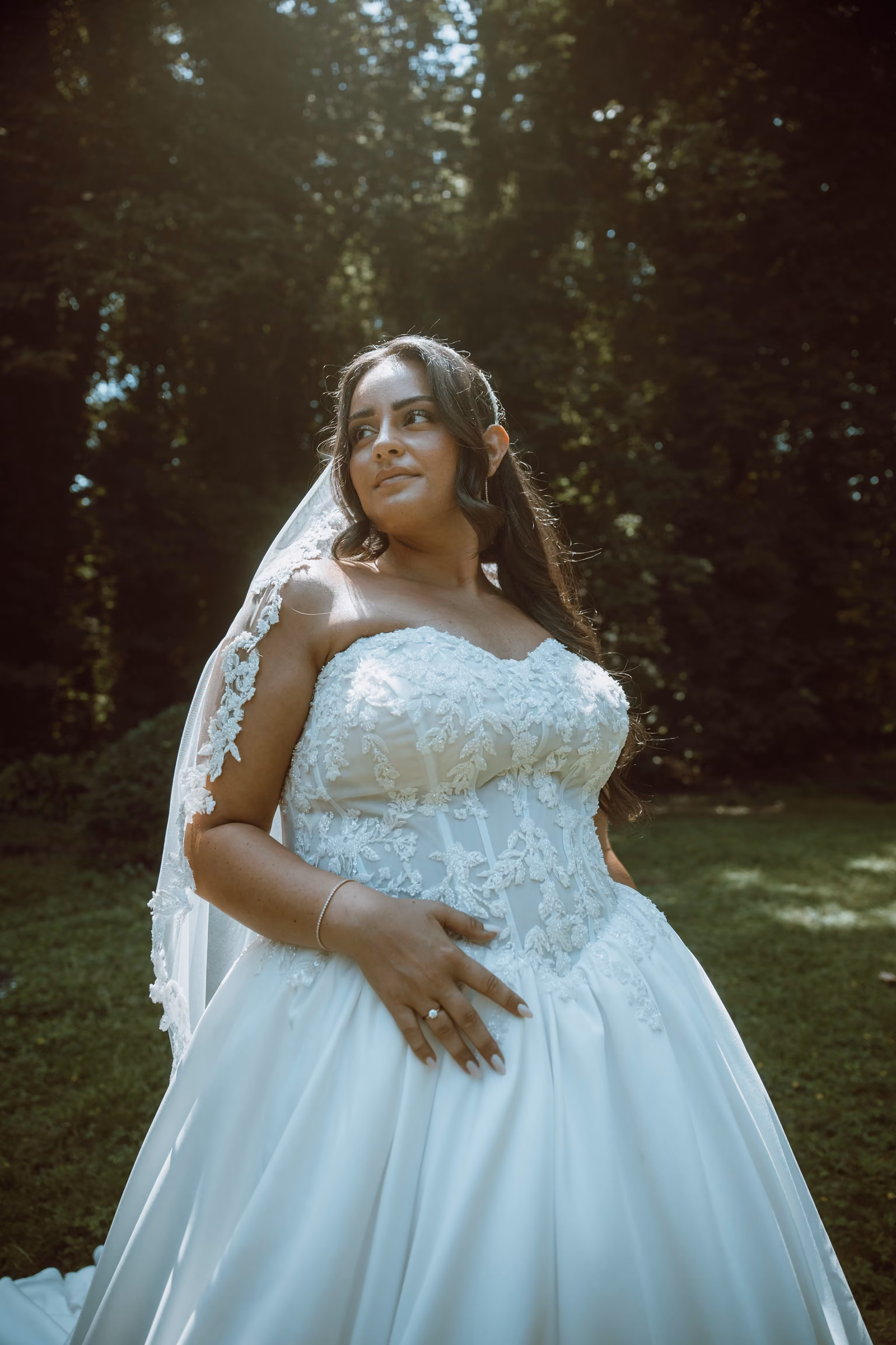 La mariée seule dans le parc, en robe de princesse, la lumière filtrant à travers les arbres