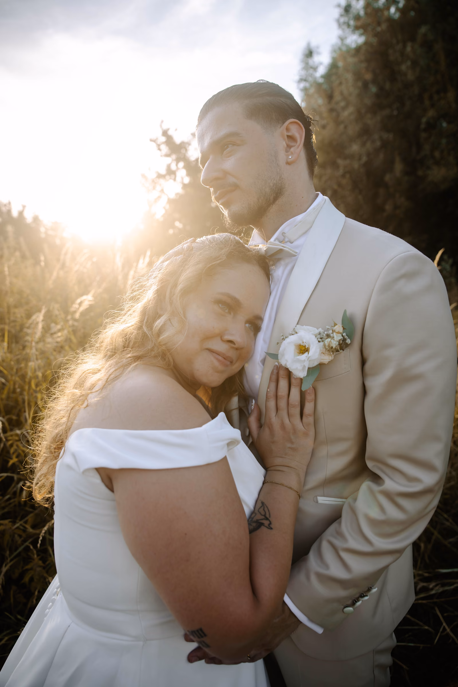 La mariée blottie contre l'épaule de son époux, le soleil couchant en contre-jour