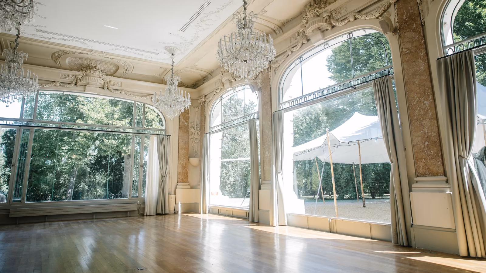 Grand salon de réception aux lustres de cristal, portes-fenêtres ouvertes sur le parc