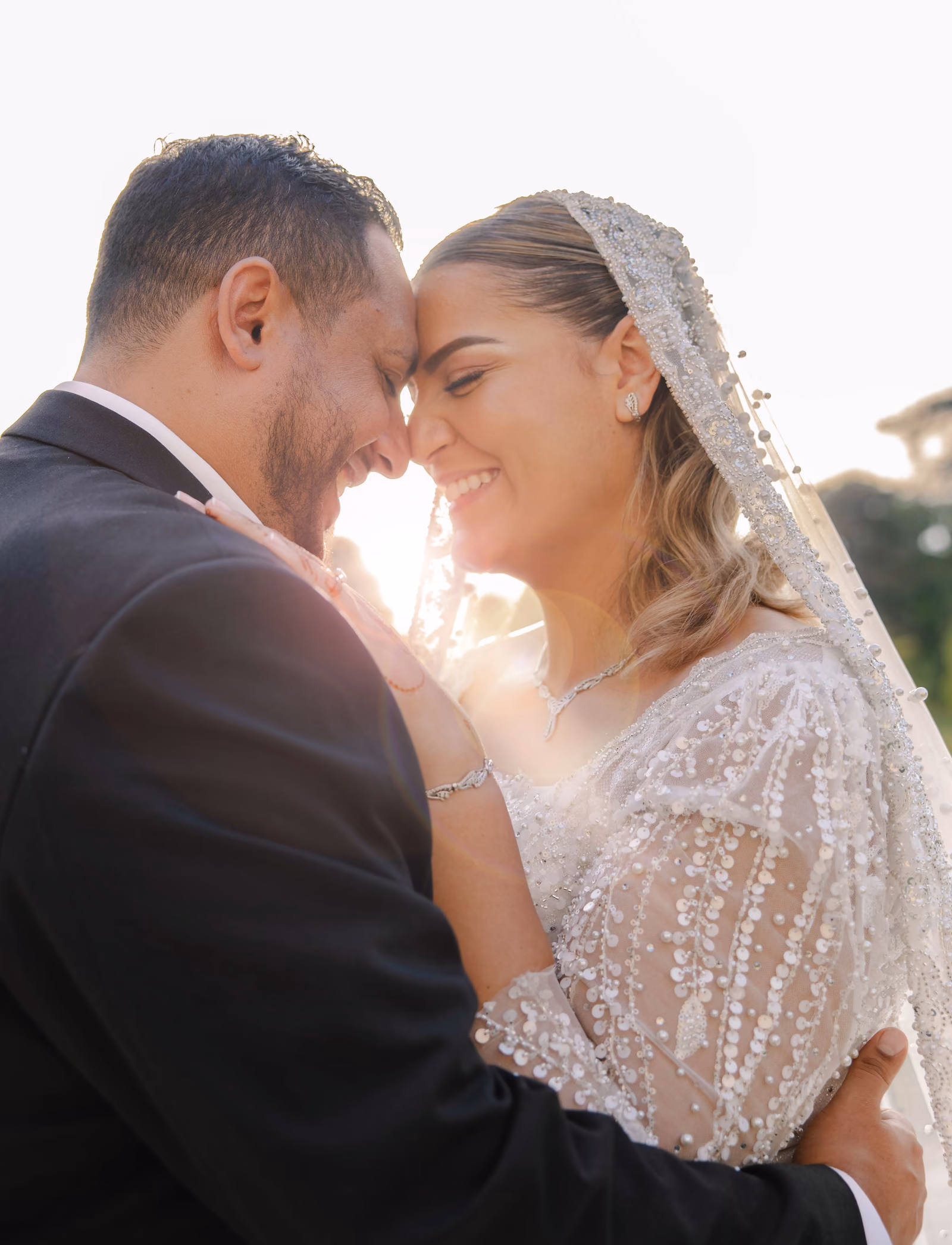 Les mariés front contre front en contre-jour, la mariée en robe brodée