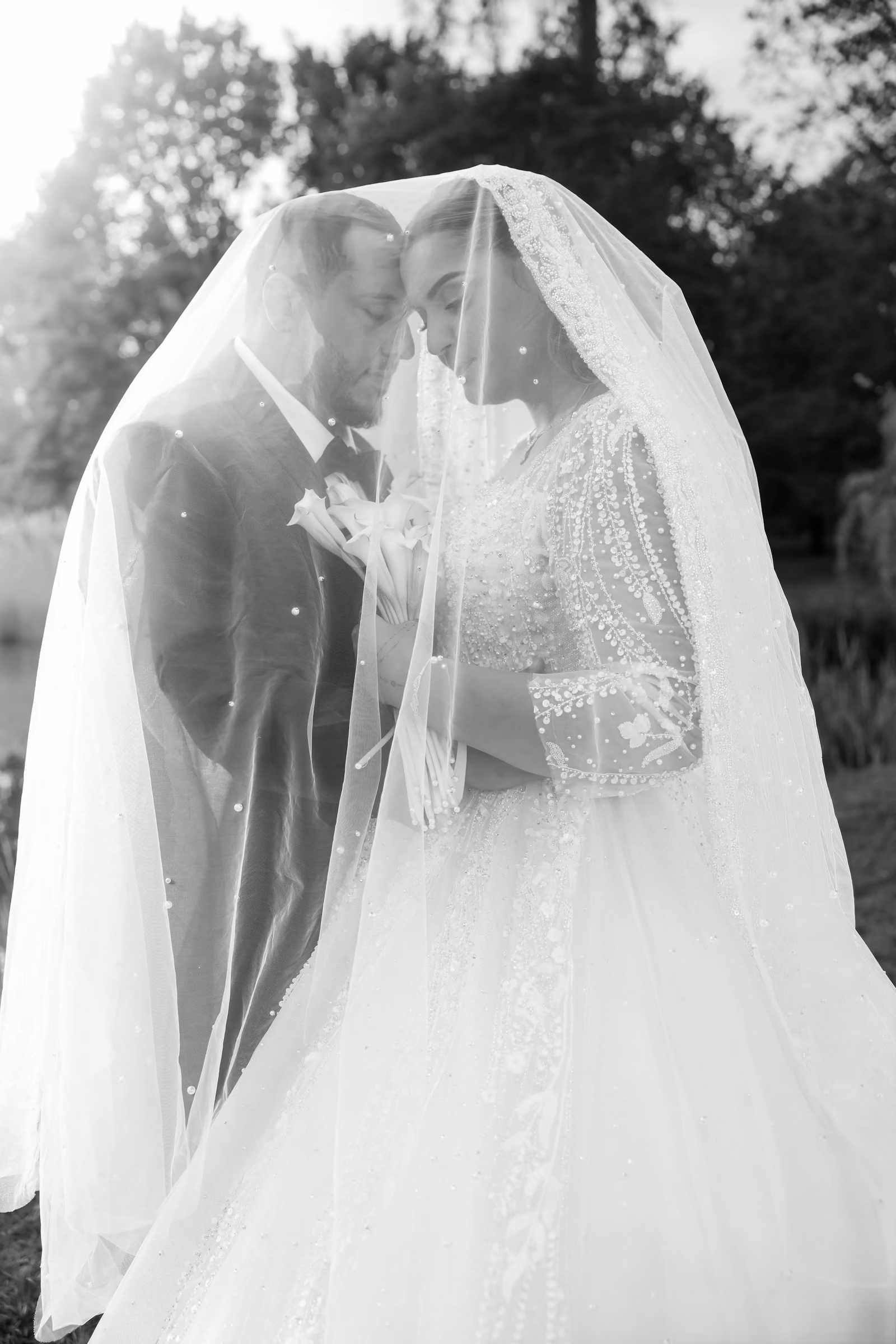 En noir et blanc, les mariés se regardent sous le voile de dentelle