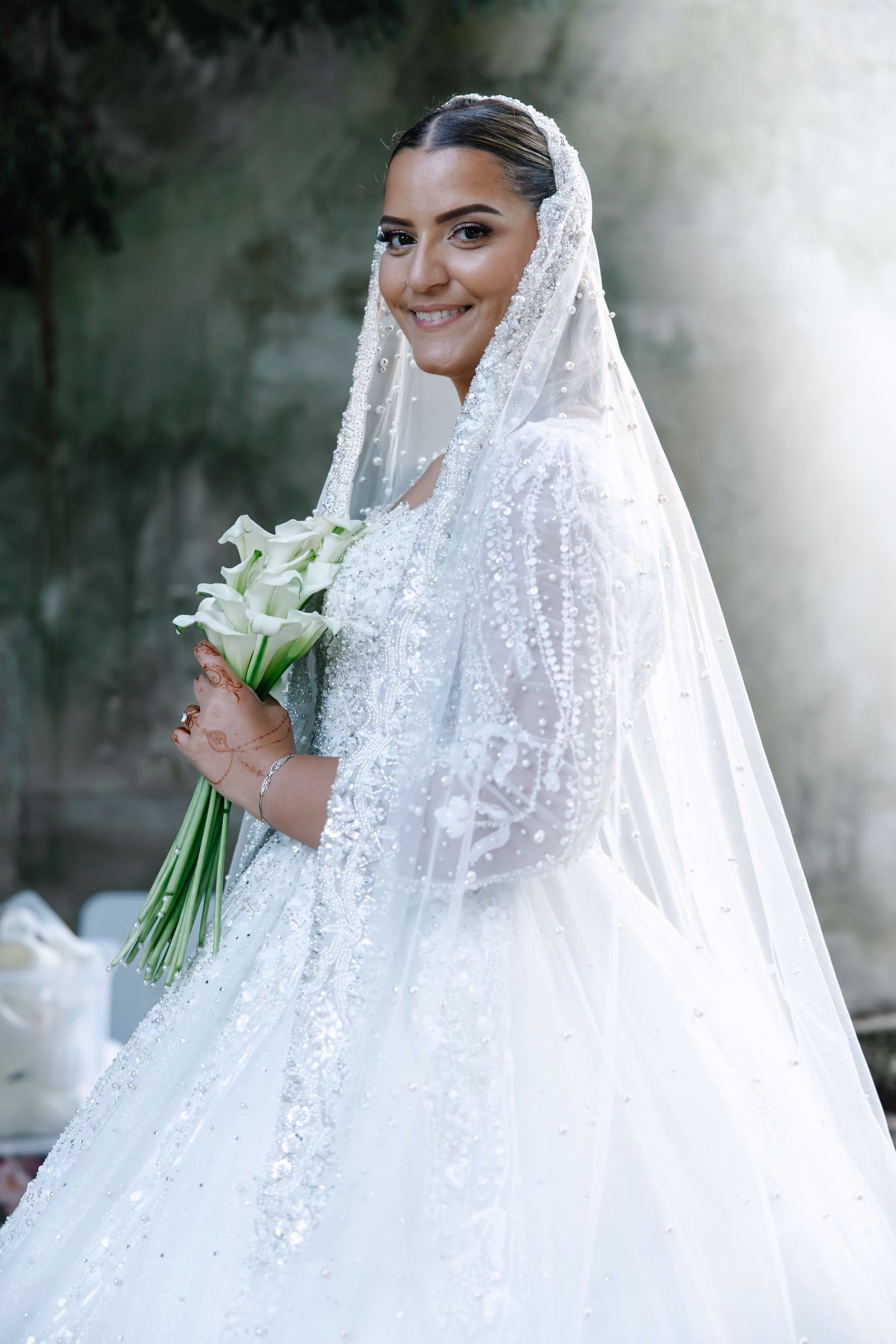 Portrait de la mariée en robe brodée, bouquet d'arums dans les bras