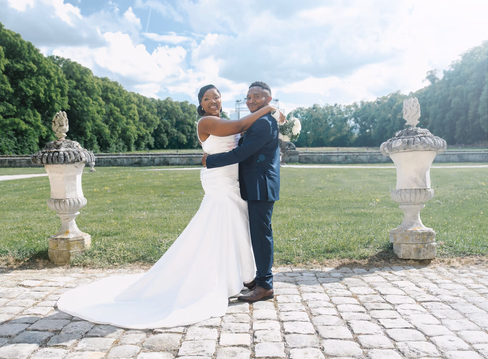 Les mariés enlacés dans les jardins du château, entre deux vasques de pierre