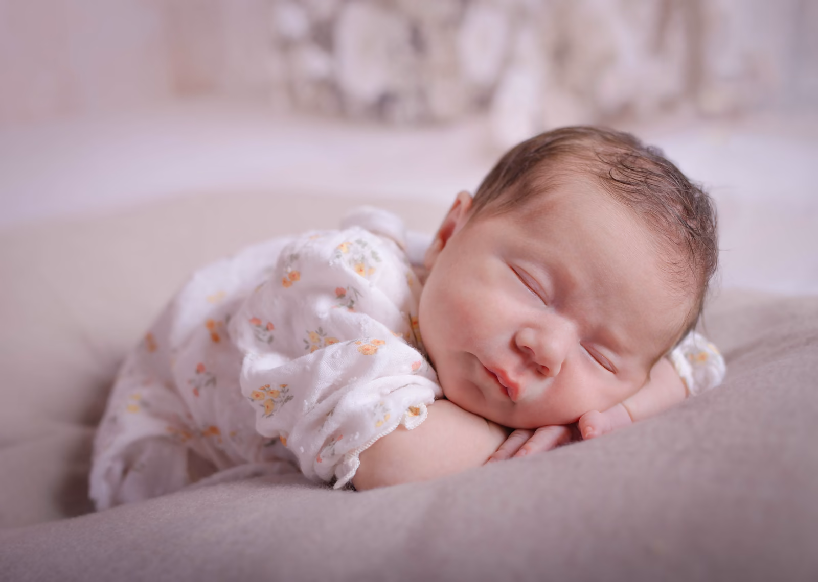 Le bébé endormi sur le ventre, en barboteuse fleurie, devant un décor blanc